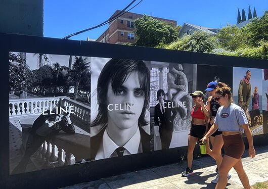 Celine wild posting on a sidewalk wall with people walking past