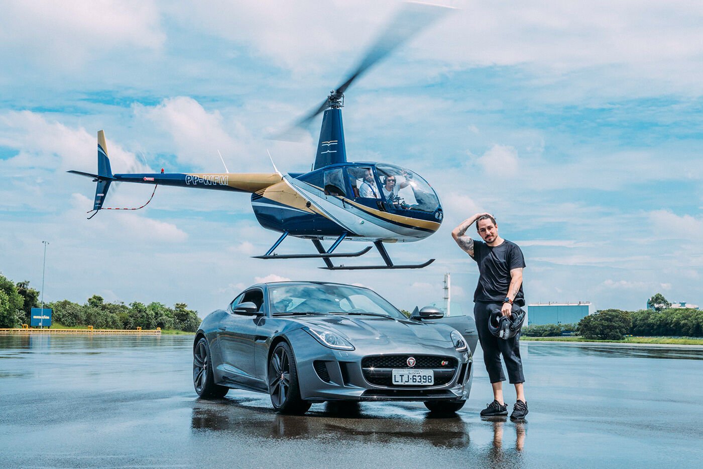A Jaguar F-Type and a helicopter on a wet test track under a cloudy sky