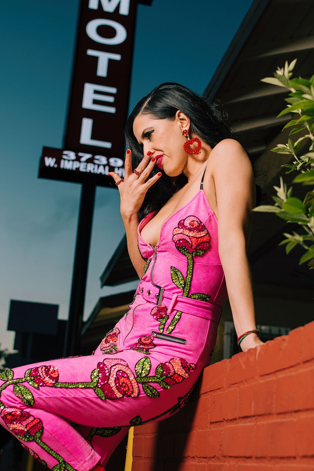 A singer in a pink rose-print jumpsuit by a motel sign in Los Angeles