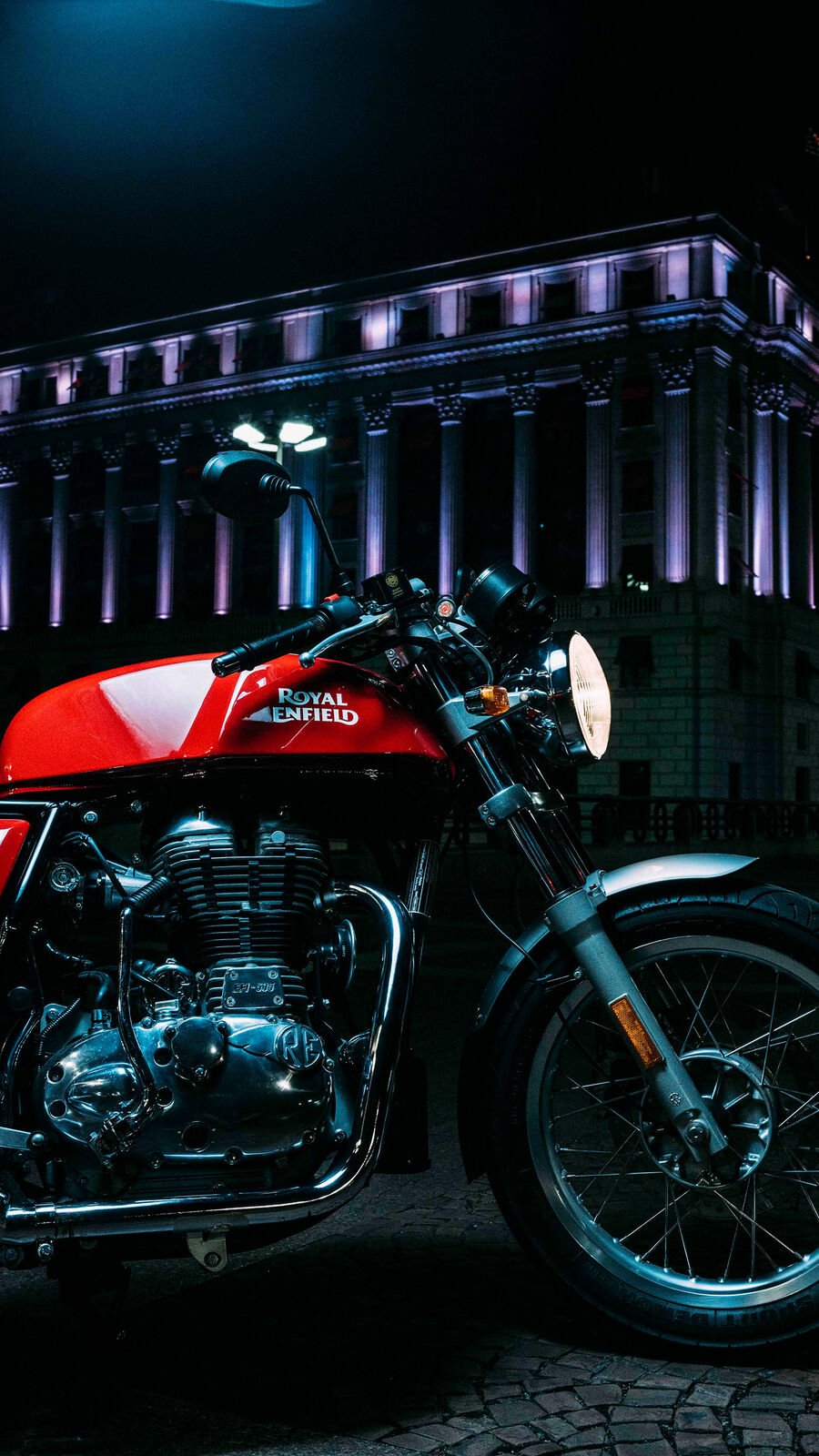 The tank and engine of a red Royal Enfield at night under blue and violet light