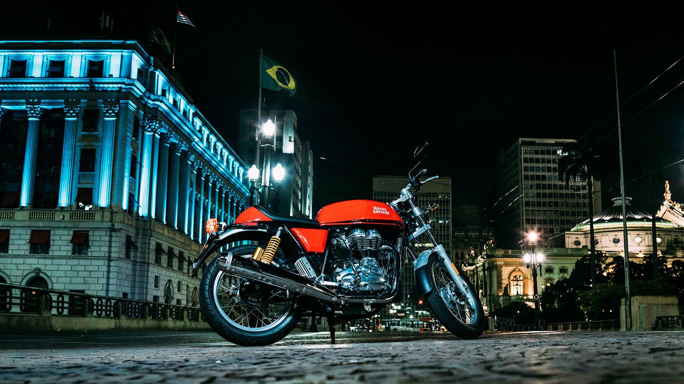 A red Royal Enfield Continental GT at night on cobblestones in front of a lit stone building in São Paulo