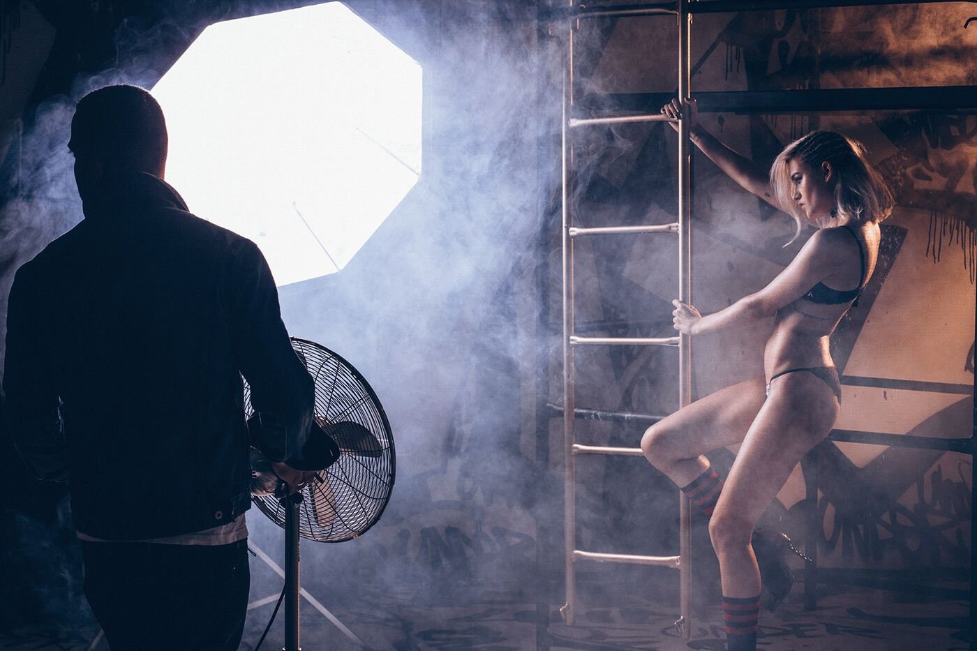 On set: a photographer lights a model on a ladder through smoke